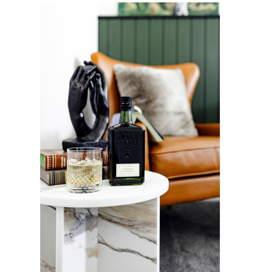 Arc Side Table with books, tan leather chair and whiskey glass and bottle